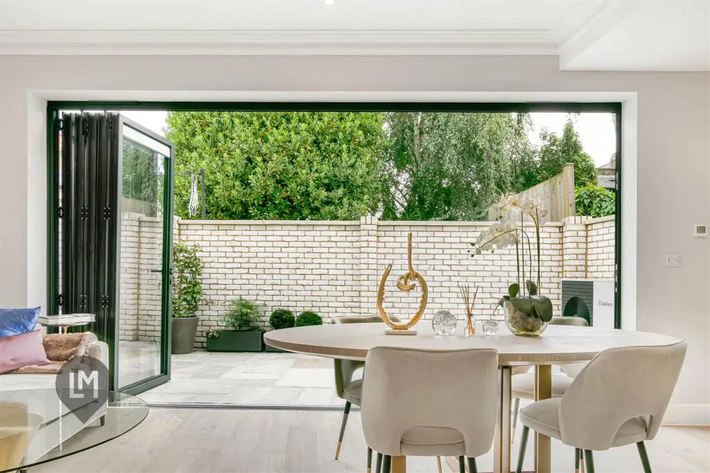 View from the dining table towards the outdoor courtyard through floor-to-ceiling glass doors in a Camborne Mews home