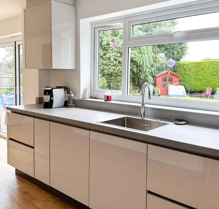 Bright kitchen with white handleless cabinets, a large window, and grey worktops