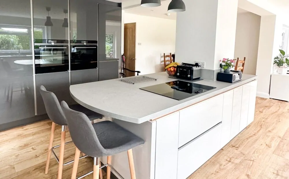 Modern kitchen view with grey high-gloss cabinets, ovens, and wooden flooring