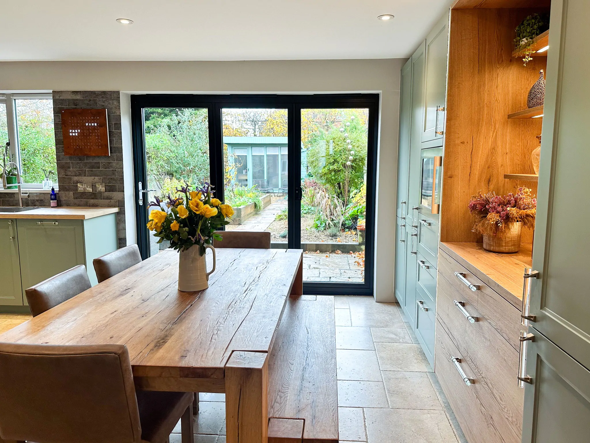 Elegant U-shaped wood shaker kitchen with green cabinets, wooden elements, and natural light