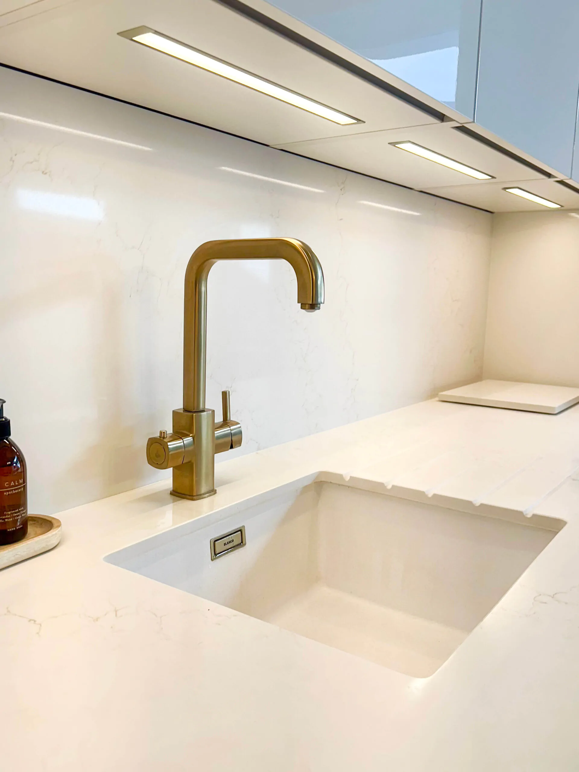 Close-up of a modern kitchen sink with a stylish golden faucet and illuminated under-cabinet lighting