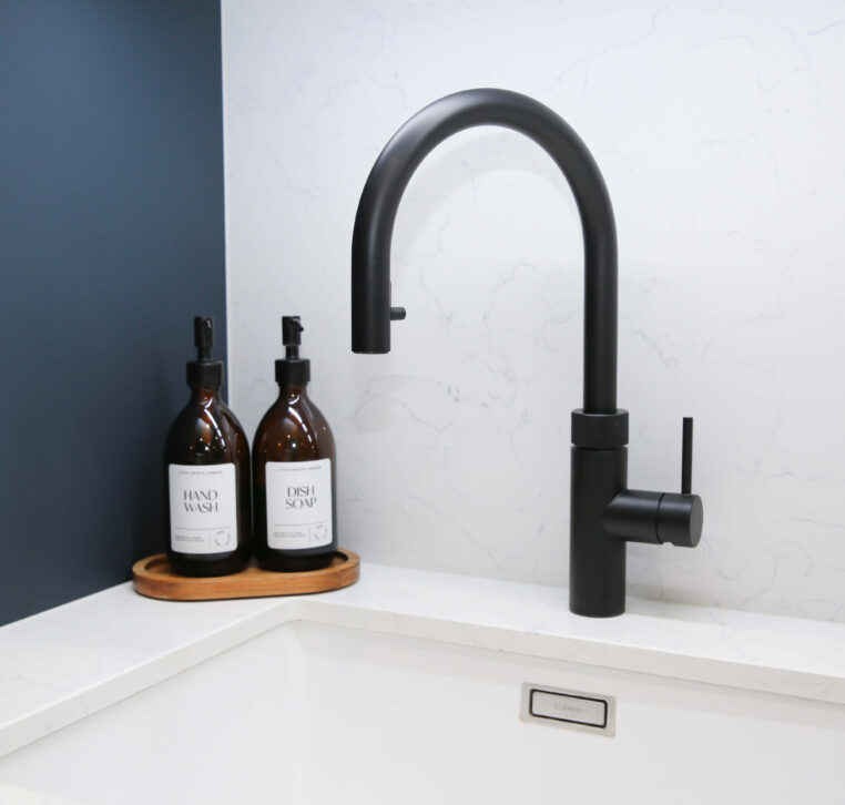 Close-up of a modern kitchen sink with a black high-arched tap and a minimalist white marble countertop
