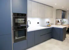 Full view of a modern L-shaped kitchen with navy blue cabinetry, double ovens, and a stylish breakfast bar