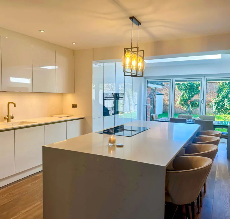 Well-lit modern kitchen with an island, golden faucet, and a large window revealing the outdoor space