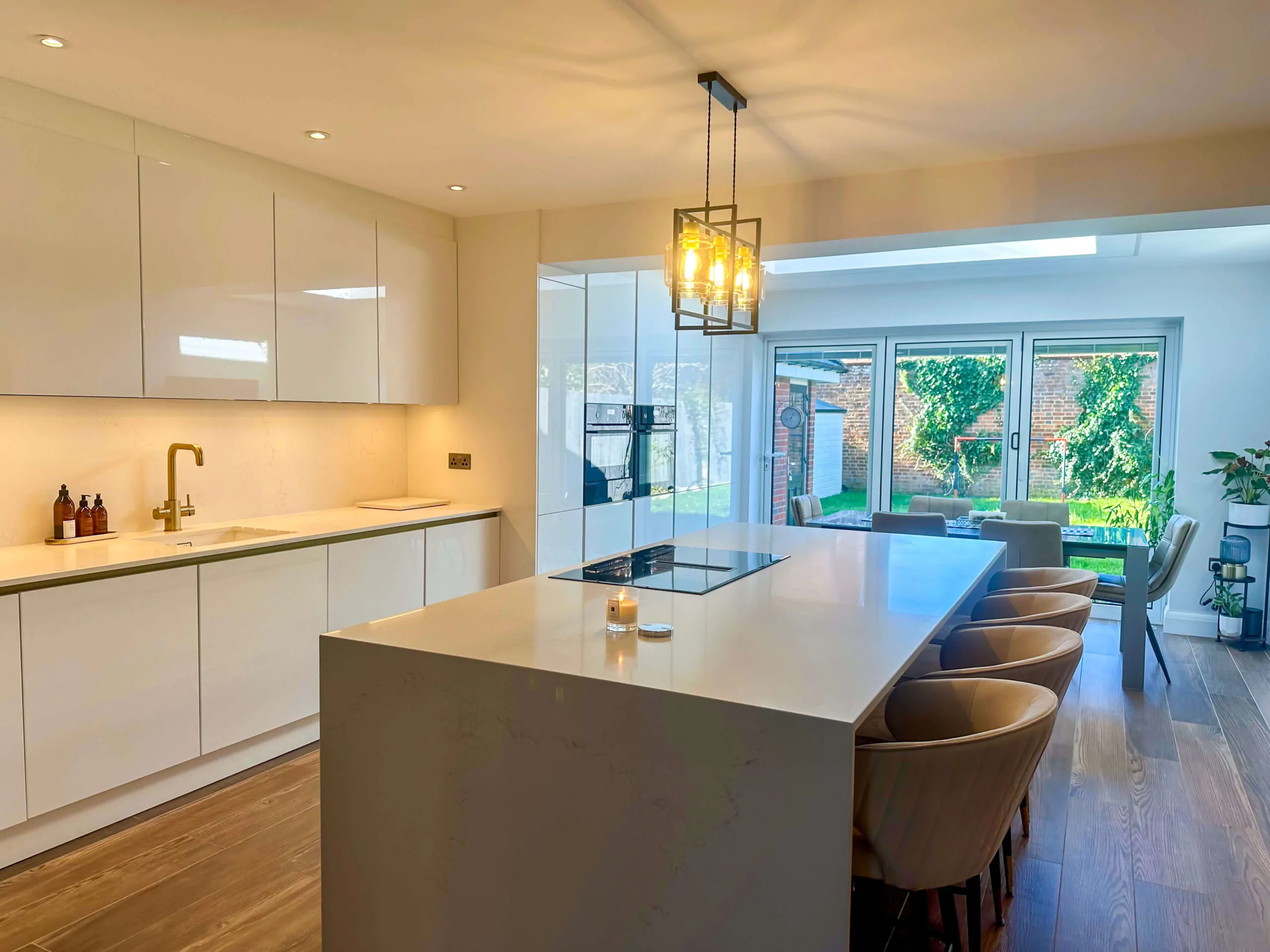 Well-lit modern kitchen with an island, golden faucet, and a large window revealing the outdoor space