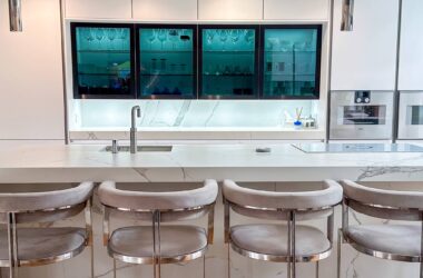 A contemporary kitchen with a glass-fronted cabinet, white marble worktops, and soft ambient lighting.