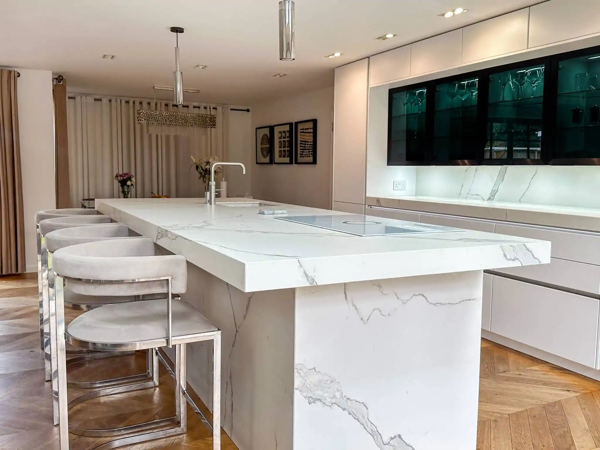 A high-end kitchen featuring a marble-clad island with seating, dark glass cabinets, and soft LED lighting.