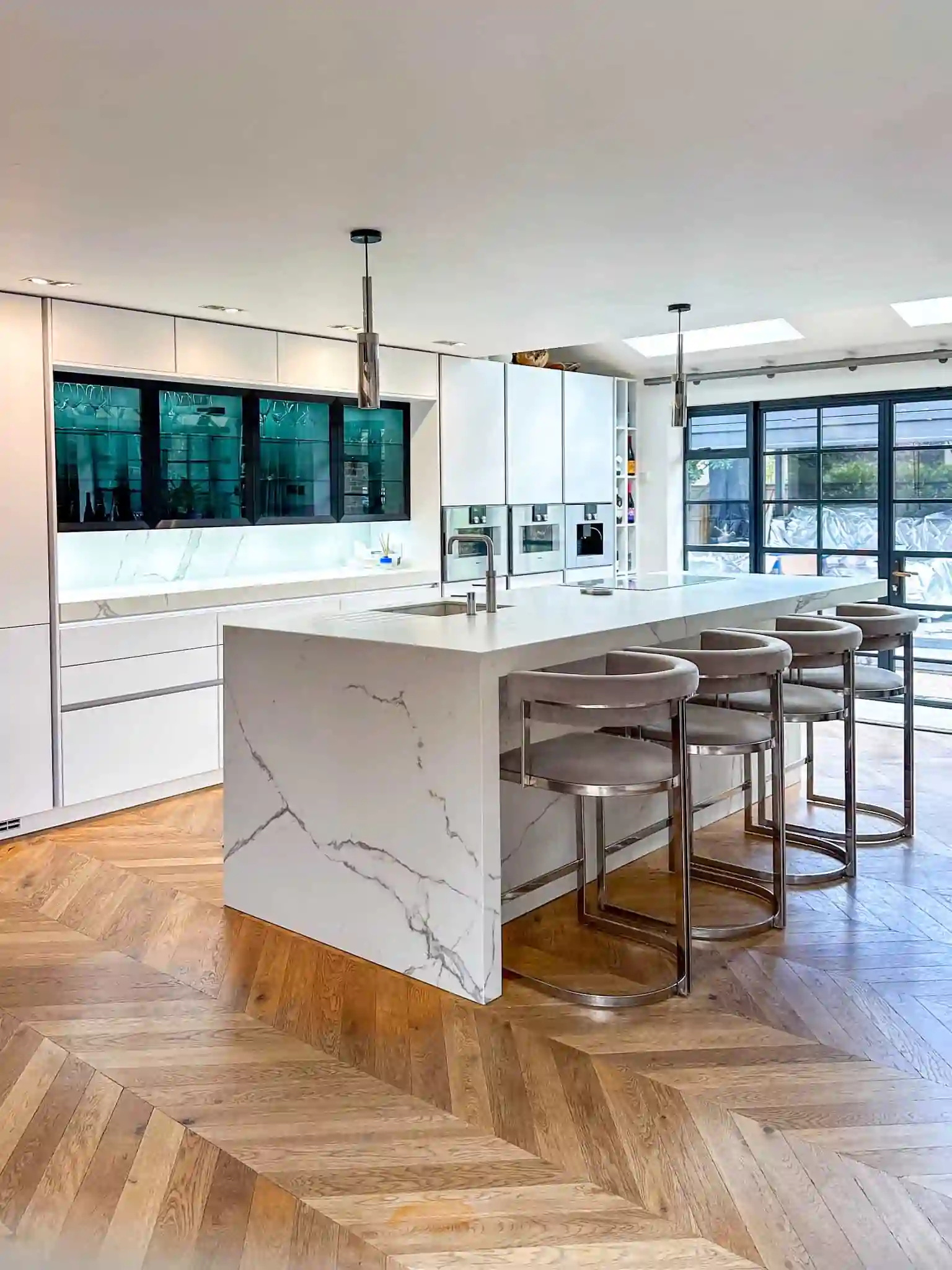 A modern kitchen with a striking marble island, chevron-patterned wooden flooring, and elegant bar stools.