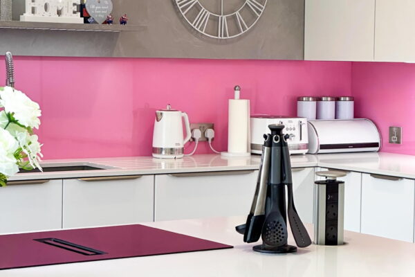 Modern white kitchen with pink backsplash featuring utensil holder and pop-up power outlets on the countertop.