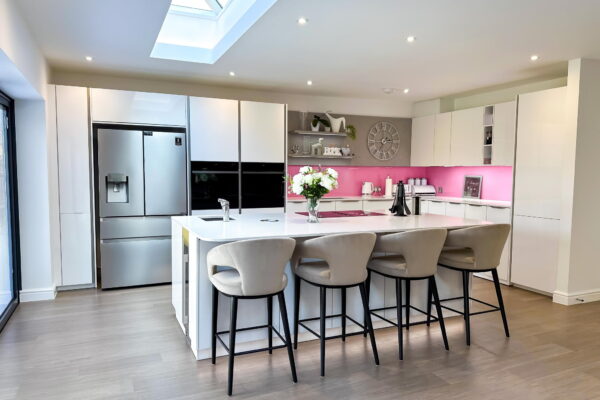 Modern White Kitchen with Pink Glass Backsplash, Spacious Island, and Integrated Appliances