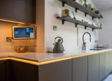 Close-up of kitchen worktop with warm under-cabinet lighting and decorative wall-mounted shelves.