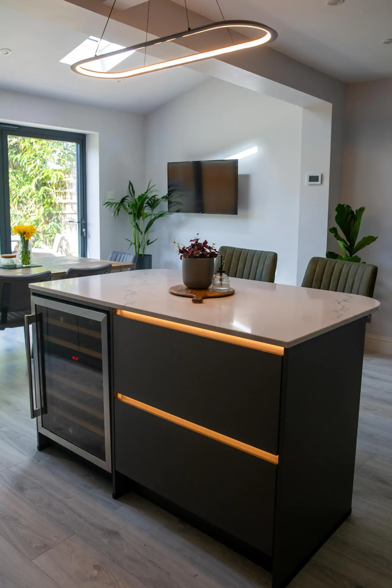 Luxury grey kitchen with modern pendant lighting, island seating, and rustic wood dining table.