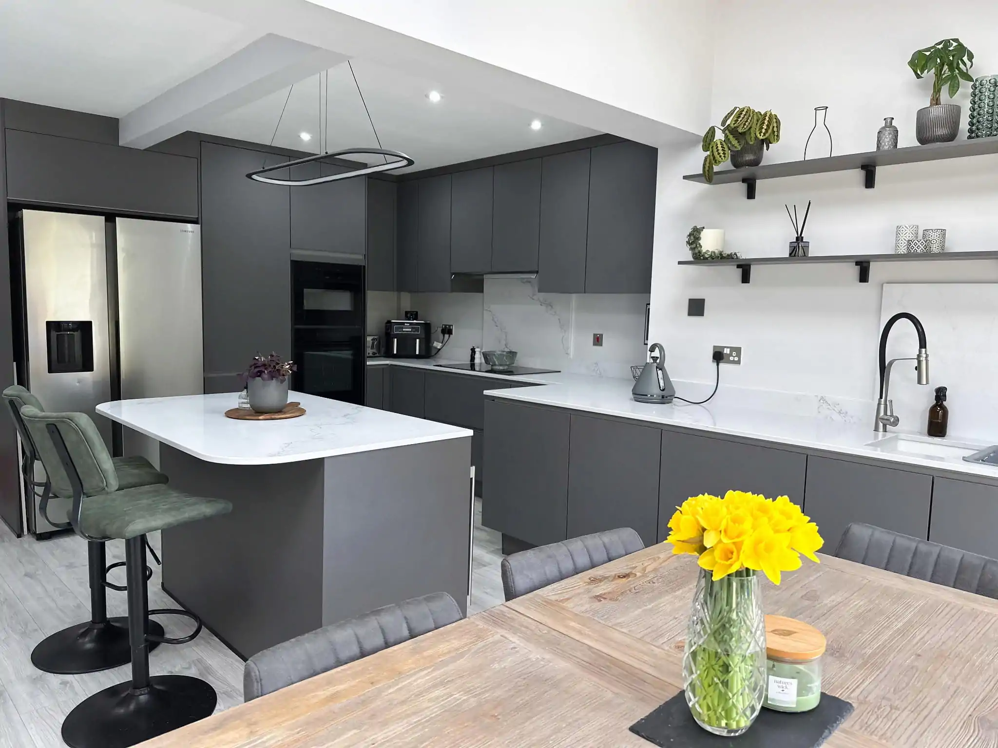 Modern grey kitchen with a white quartz island, open shelving, and dining area with large garden doors.
