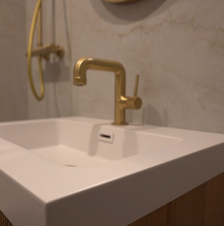 Detail shot of a contemporary brushed gold basin mixer tap on a white countertop sink with wood vanity.