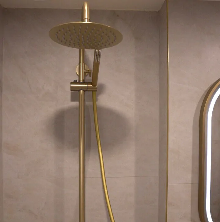 Close up of a luxury brushed gold rain shower head and riser rail against marble effect wall tiles.