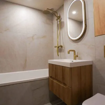 Completed bathroom renovation showing the bathtub, fluted wood vanity, and brushed gold shower set.