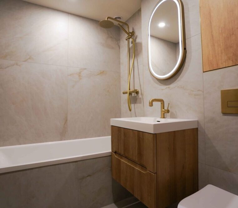 Completed bathroom renovation showing the bathtub, fluted wood vanity, and brushed gold shower set.