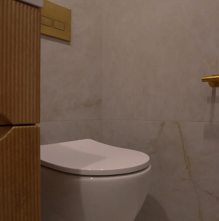Modern wall-hung white toilet featuring a brushed gold dual flush plate and fluted wood vanity unit.