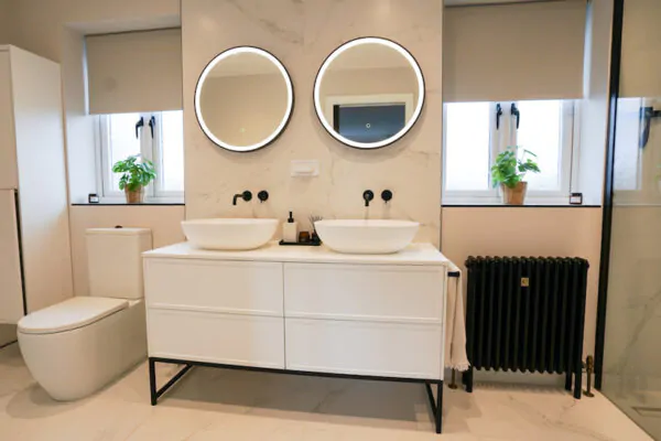 Double vanity unit with round LED backlit mirrors and wall-mounted taps.