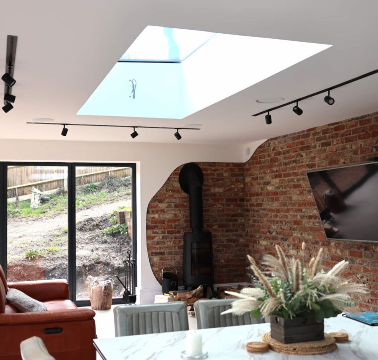 Open plan kitchen dining and living space with skylight, exposed brick wall and wood burner