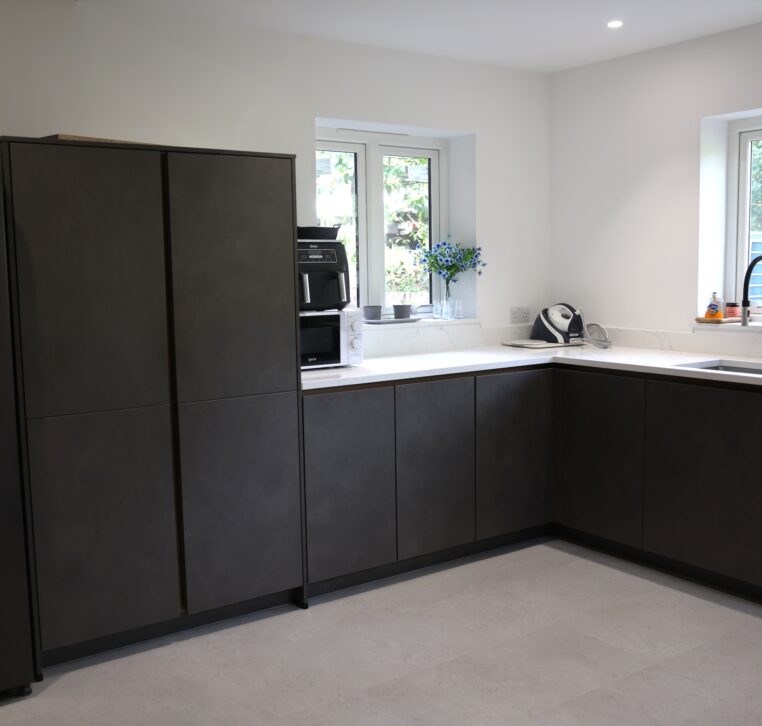 Modern kitchen with dark handleless units and L-shaped worktop with sink and windows