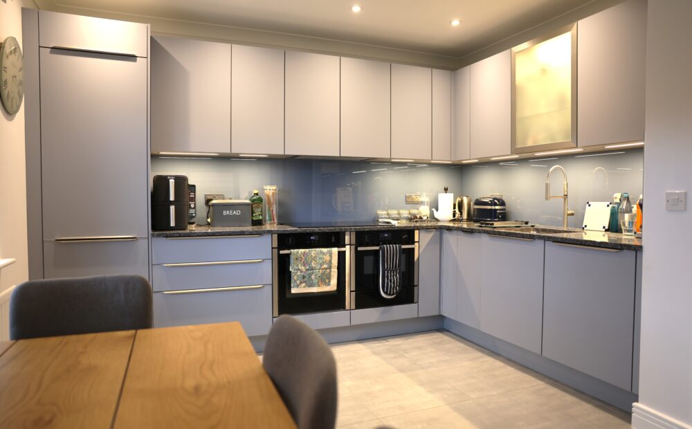 Contemporary grey handleless kitchen with stone worktops, glass splashback and integrated appliances