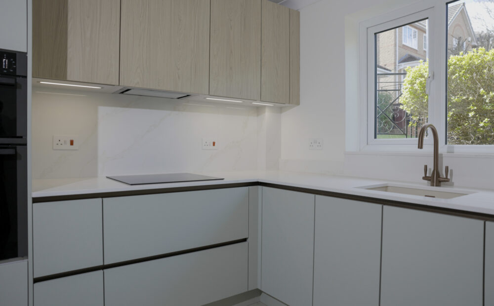 L-shaped modern kitchen with handleless cabinets, integrated hob and marble-effect splashback