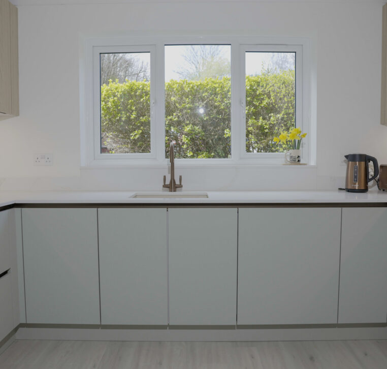 Modern white kitchen with handleless cabinets, integrated sink and large window providing natural light