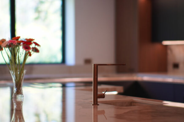 Modern kitchen featuring a marble countertop with copper tap and fresh flowers, designed and installed by MAS Kuchen.