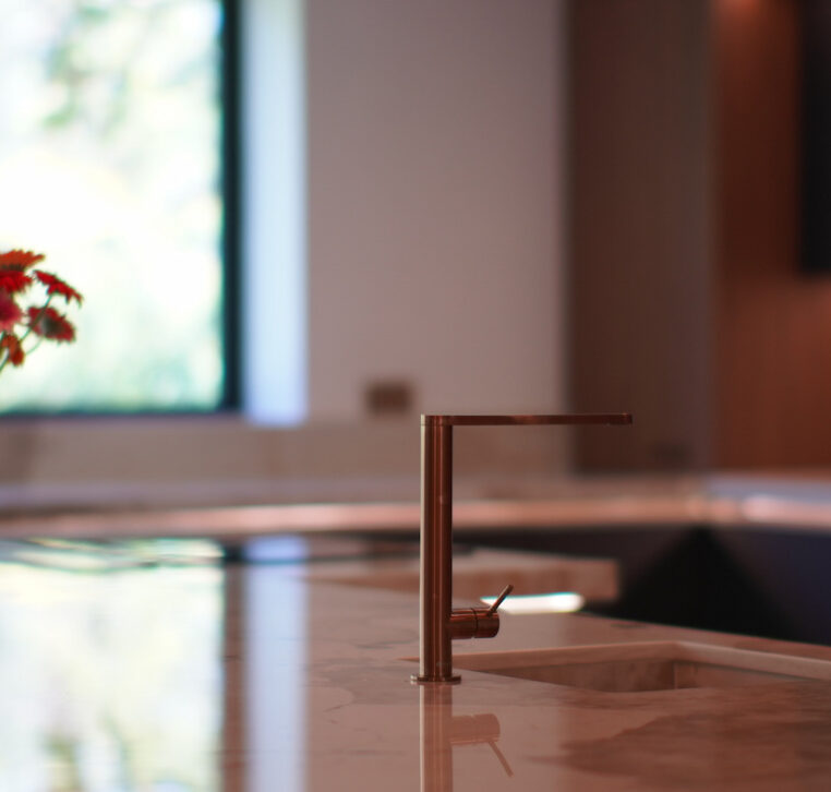 Modern kitchen featuring a marble countertop with copper tap and fresh flowers, designed and installed by MAS Kuchen.