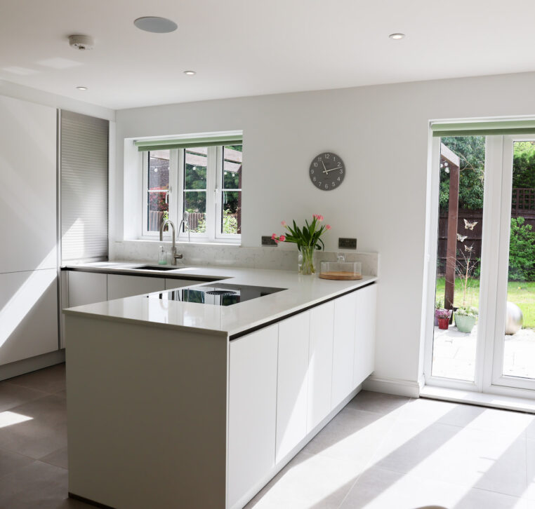 Open-plan white kitchen with garden doors, handleless cabinetry, light worktops and integrated appliances