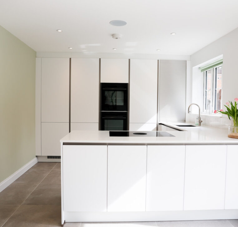 White handleless kitchen with integrated black ovens, light worktops and built-in storage