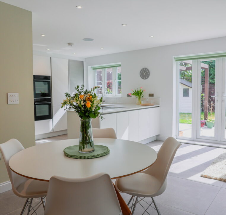 White handleless open-plan kitchen with dining area, garden doors and light neutral finishes